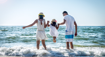 Two parents swing child by arms on beach